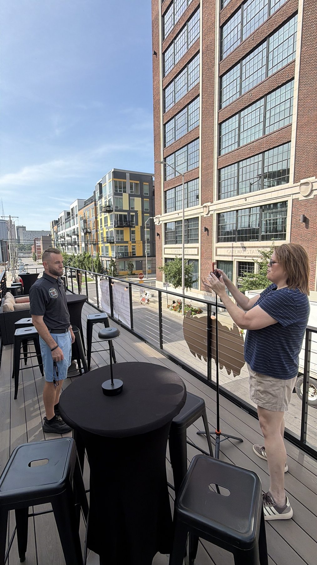 Two people talking on the lounge rooftop deck beside a high-top table on a sunny afternoon
