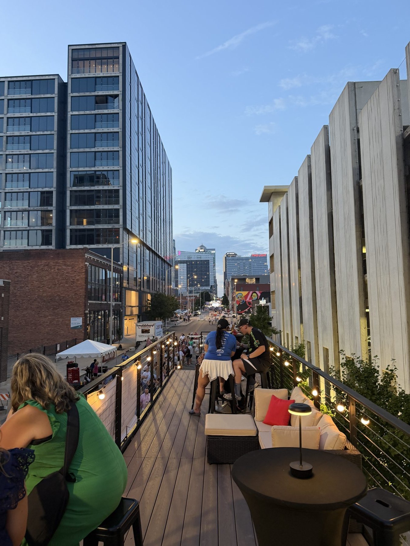 Guests on the lounge rooftop at dusk, looking down a city street lined with lights and buildings