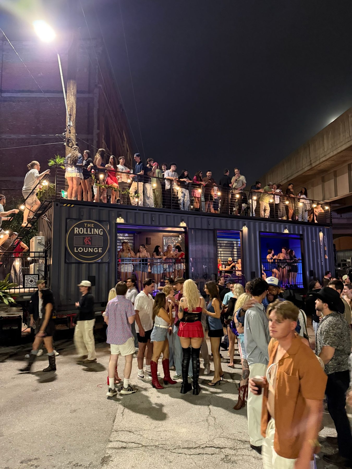 A packed evening event around The Rolling Lounge with guests inside and on the roof